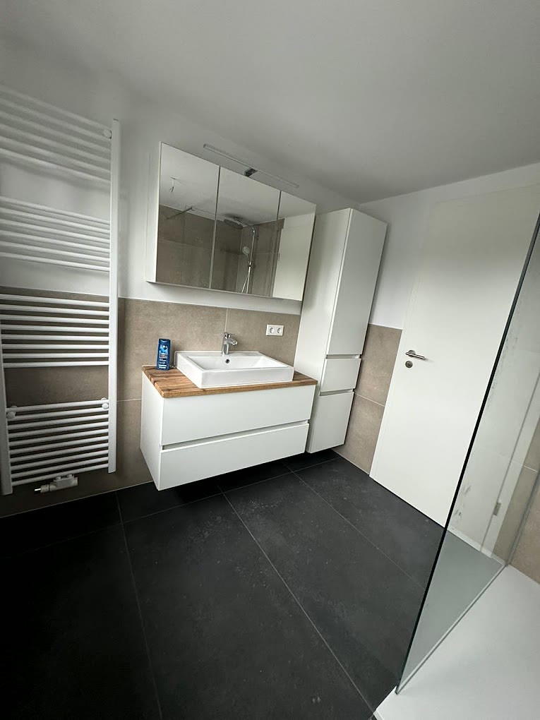 Modernes Bad mit weißem Waschtischunterschrank, Eichen-Holzplatte, Aufsatzbecken, Spiegelschrank und anthrazitfarbenem Fliesenboden.