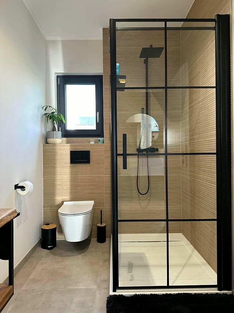 Dusche mit schwarzer Glastür im Sprossen-Raster, Holzoptik-Fliesen, wandhängendem WC und mattschwarzen Armaturen.