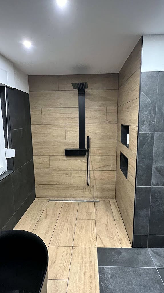 Ebenerdige Dusche mit Holzoptik-Fliesen, dunklem Schiefer, mattschwarzer Regendusche und Linienablauf.